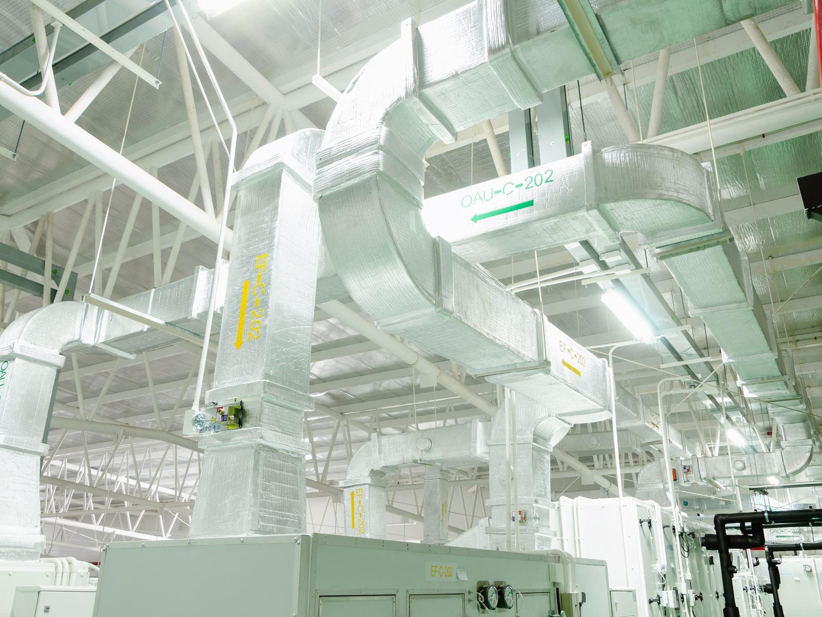 Weiße Lüftungskanäle und ein RLT-Gerät in einer hellen Industriehalle